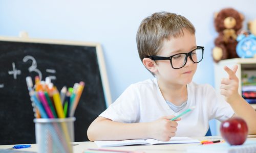 7 years old boy solves multiplication table in his copybook and counting on fingers. Back to school